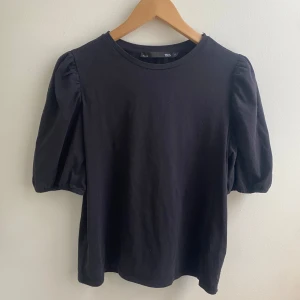 Svart topp med puffärmar - Snygg svart topp med puffärmar och rund halsringning. Perfekt för en stilren look. Tillverkad i mjukt material för extra komfort.