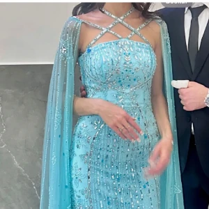 Turkos glittrig långklänning - Elegant turkos långklänning med glittriga detaljer och korsade axelband. Klänningen har en tight passform och är perfekt för festliga tillfällen. pärlor kan ha ramlat av. Använt endast en gång, mitt pris 2999 kr. Pris kan diskuteras. Storlek 32 men jag som har har storlek 34-36 passar den perfekt. Färgen är som på första bilden, dvs turkos.