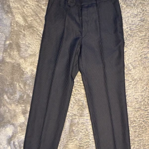 Marinblå randiga kostymbyxor - Marinblå kostymbyxor med diskreta ränder och lågmidjade.  70cm midja,Innerbenslängd 76cm. 106cm ytterbenslängd med 22cm benöppning