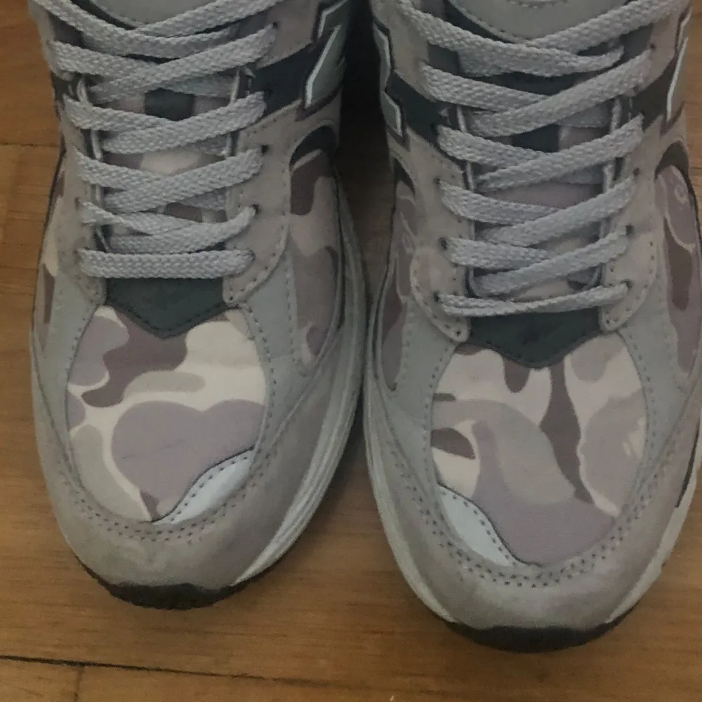 Snygga grå sneakers från New Balance med ett coolt camouflagemönster (BAPE). Skorna har en bekväm sula, perfekt för en avslappnad stil. Använda ett flertal gånger, tycker om dem men behöver lite extra pengar. Priset är ej hugget i sten. Kengät.