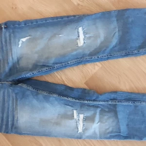Blå jeans med slitningar från LAB Industries - Snygga blå jeans med slitningar för en trendig look. De har en regular fit och är perfekta för en avslappnad stil. Jeansen har klassiska fem fickor och knappar i midjan.
