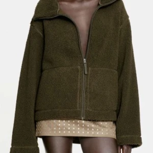 Ny mörk khakigrön teddyjacka från H&M - Ny och oanvänd med etikett kvar.. Mysig mörkgrön pilejacka med hög krage och dragkedja framtill. Perfekt för kyliga dagar med sin mjuka och varma känsla. Jackan har en avslappnad passform och långa ärmar. Storlek L (ej oversized). HM