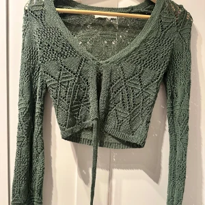 Grön stickad kofta från Pull&Bear - Säljer en snygg grön stickad kofta från Pull&Bear. Den har ett vackert mönster och knytning framtill. Perfekt för lager-på-lager och att ge en bohemisk touch till din outfit.