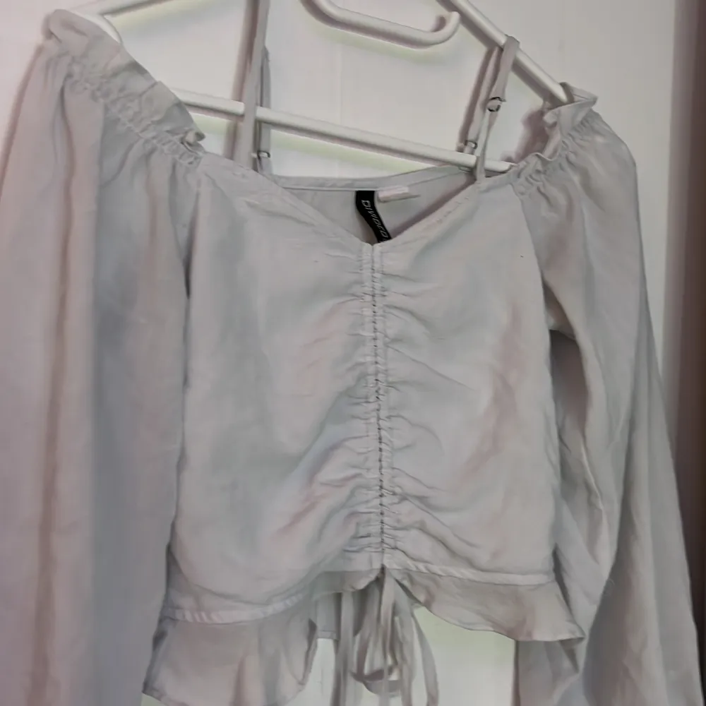 Säljer en vit offshoulder blus från H&M Divided. Toppen har långa ärmar med resår vid ärmsluten och en snygg knytning framtill. Perfekt för en trendig look! Blusen ser grå ut på bilden men den är vit!!💞. Puserot.
