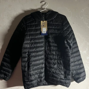 Svart dunjacka - Säljer en helt ny dunjacka från Stormberg.  Perfekt för kyligare väder med sin quiltade stil och huva. Nypris 399