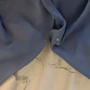 Blå bodysuit - Snygg blå ärmlös bodysuit med djup v-ringning och en knapp i v ringningen. Perfekt för en stilren look. Tillverkad i ett mjukt och bekvämt material.