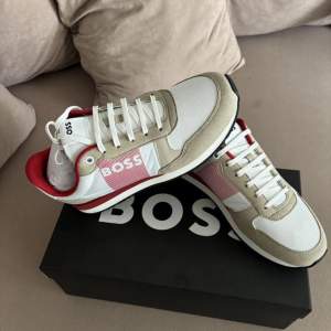 Snygga Boss sneakers i beige och röd färg. Perfekt för vardagligt bruk eller för att klä upp en outfit. jag säljer Hugo Boss Skor Helt Nytt Nypris 1877 kr Storlek 41 oanvänd (priset kan diskuteras)