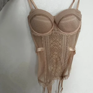 Beige spetskorsett - En superfin beige korsett med spetsdetaljer som är oanvänd. Den har justerbara axelband och en snygg snörning bak. BH storlek B/C.