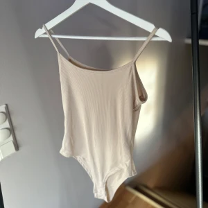 Beige ribbad body - Snygg beige bodysuit med smala axelband och ribbad textur. Perfekt för sommardagar eller som basplagg under en kavaj. Den är i mycket bra skick, använd 1 gång 