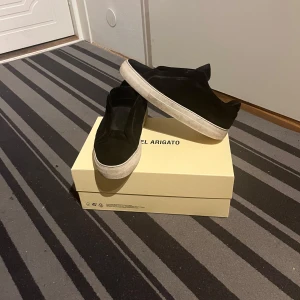  Arigatos 360 laceless  - Säljer ett par stilrena svarta sneakers från Axel Arigato. De har en klassisk design med vit sula och är perfekta för vardagsbruk. Skorna är i bra skick och kommer i originalkartong. Perfekta för både höst och vår!