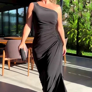 Svart långklänning med slits - Elegant svart långklänning med en smickrande drapering och glittriga detaljer vid midjan. Klänningen har en stilren slits som ger en sofistikerad look. Perfekt för festliga tillfällen!Helt ny