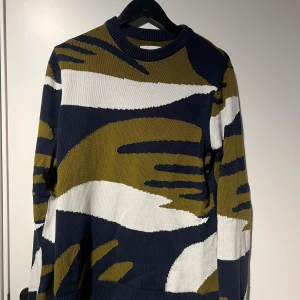 Mönstrad stickad tröja från samsoe samsoe  - Säljer en cool stickad tröja med ett unikt mönster i olivgrön, marinblå och vit. Perfekt för att sticka ut i mängden! Tröjan har långa ärmar och en bekväm passform. Perfekt för höst och vinter.