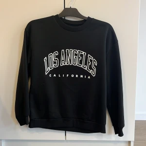 Svart sweatshirt med Los Angeles-tryck - Säljer en svart sweatshirt med texten 'Los Angeles California' i vitt på framsidan. Tröjan har en klassisk rund hals och långa ärmar, perfekt för en avslappnad stil. Den är i bra skick. 🖤