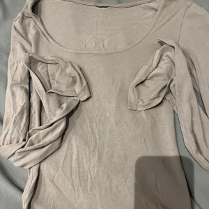 Beige långärmad topp från Gina - Säljer en stilren beige långärmad topp i mjukt material. Perfekt för både vardag och festliga tillfällen. Toppen har en rund halsringning och är i bra skick. Passar utmärkt till höst- och vårgarderoben.