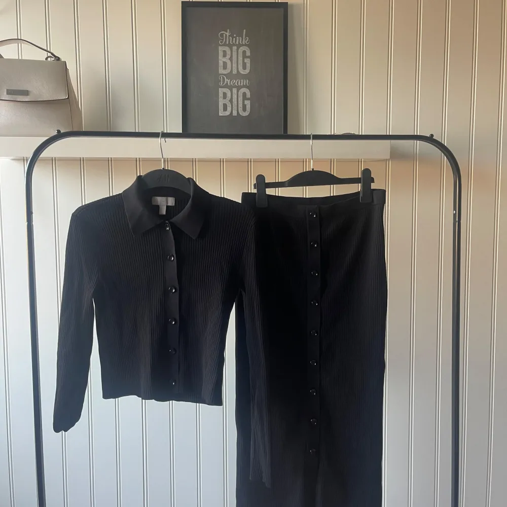 Snygg svart ribbad kjol med knappar framtill. Perfekt för både vardag och fest. Kjolen är i ett stretchigt material som ger en bekväm passform. Matcha med en stilren topp för en komplett look!. Hameet.