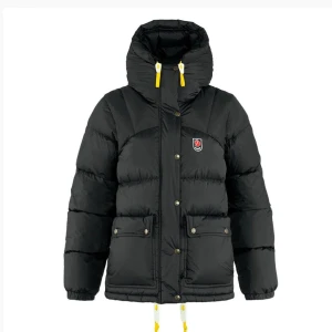 Svart dunjacka från Fjällräven - Säljer en snygg och varm svart dunjacka från Fjällräven. Jackan har en pufferstil med långa ärmar och praktiska fickor framtill. Den har en dragkedja och knappar för extra skydd mot kylan. Perfekt för vinterns kalla dagar! 🖤