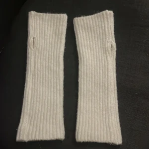 Vita stickade handledsvärmare - Säljer ett par vita stickade handledsvärmare. De är ribbstickade och har en öppning för tummen, vilket gör dem perfekta för att hålla händerna varma samtidigt som du kan använda fingrarna. Perfekta för kyliga dagar! 