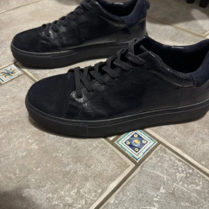 Kurt Geiger skor - Säljer ett par mörkblåa sneakers från kurt Geiger i bra skick. De har en stilren design med snörning och en kombination av mocka och glansigt material. Perfekta för både vardag och fest! Storlek herr 43. Ny pris: 2000