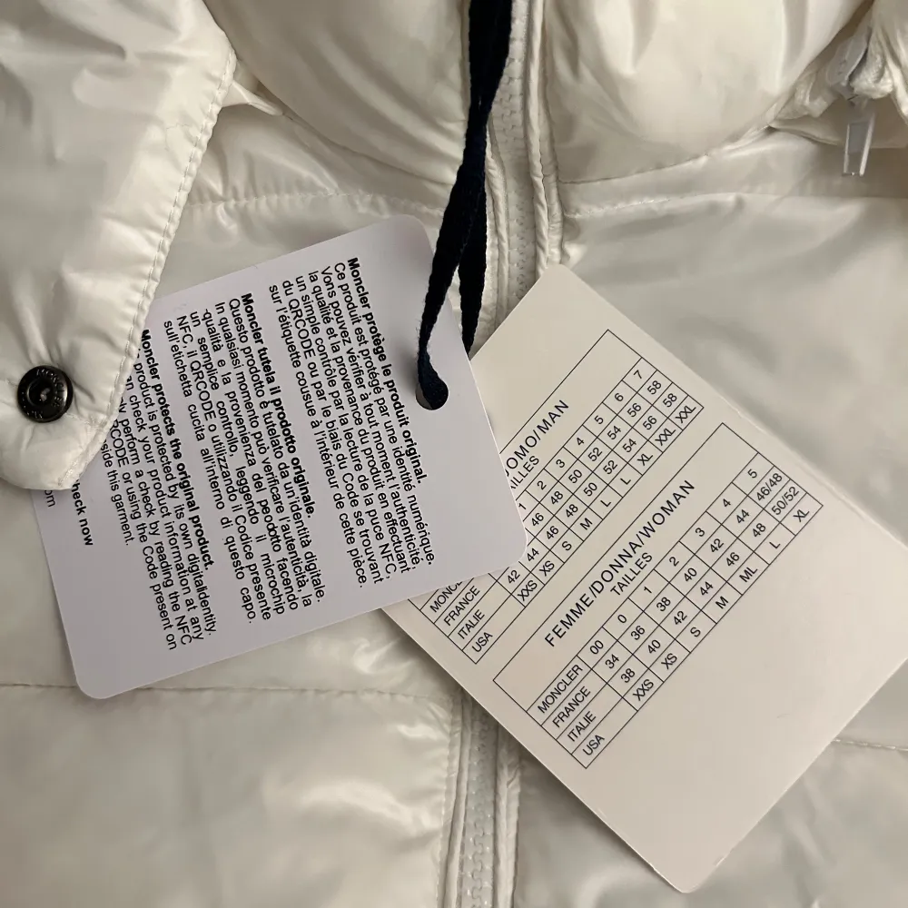 Säljer en snygg vit dunjacka från Moncler i storlek L. Jackan har en quiltad design med dragkedja och knappar. Den är perfekt för vintern med sin varma och stilrena look. Moncler-loggan finns på ärmen. Passar både till vardags och festliga tillfällen!. Takit.