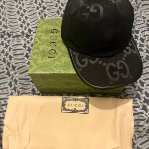 Svart keps från Gucci - Säljer en svart keps från Gucci i nytt skick. Kepsen har ett stilrent GG-mönster och justerbar rem baktill. Perfekt för att ge din outfit en lyxig touch. Levereras med originalförpackning och etiketter.