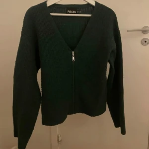 Mörkgrön kofta från Pieces - Säljer en snygg mörkgrön kofta från Pieces i storlek S. Den har en dragkedja framtill och är ribbad vid ärmslut och nederkant. Perfekt för höst och vinter, supermysig och lätt att matcha med andra plagg. Passar både till vardags och lite finare tillfällen. 🍂