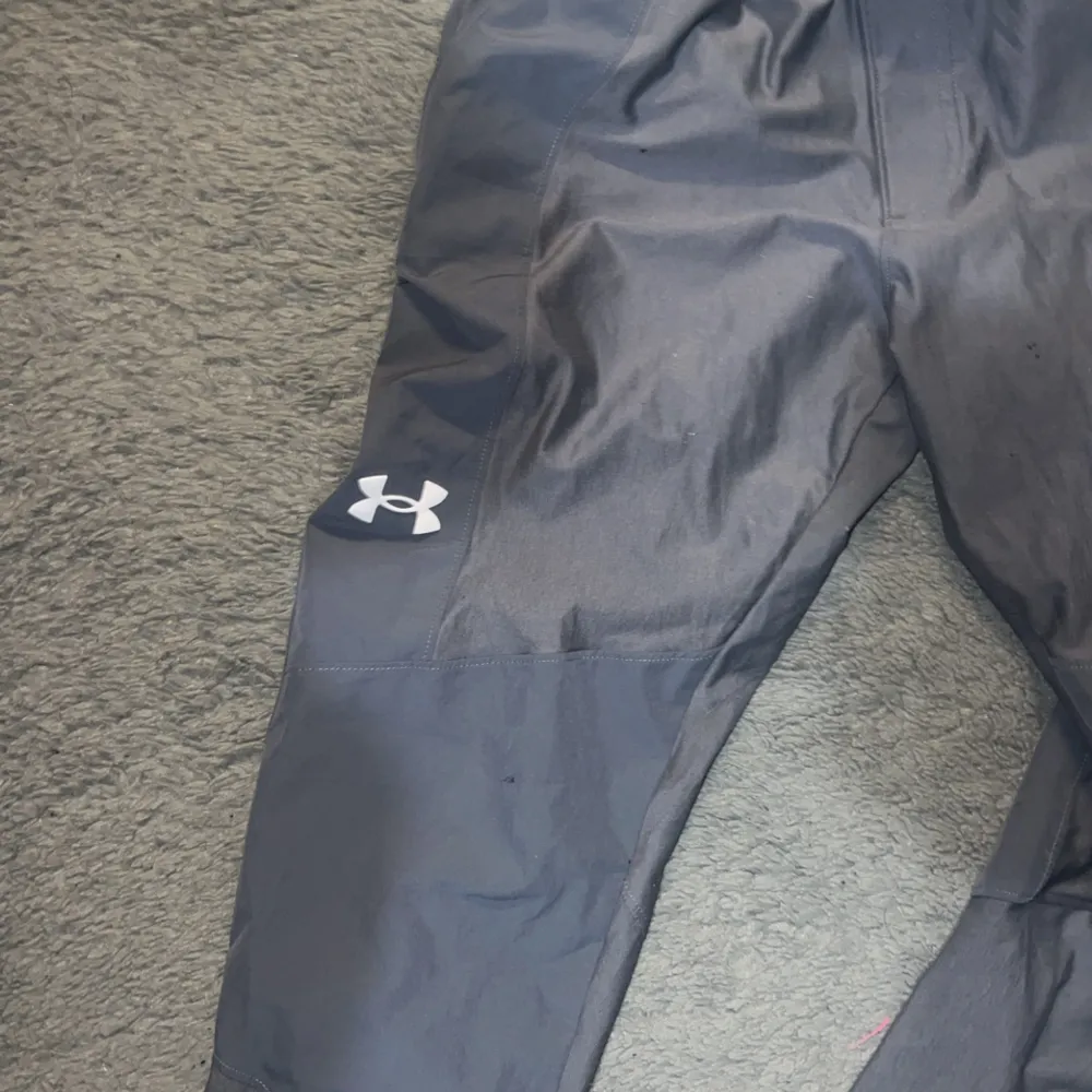 Säljer ett par grå träningsbyxor från Under Armour i bra skick. De har en elastisk midja och är perfekta för träning. Byxorna är tillverkade i ett lätt och bekvämt material, vilket gör dem idealiska för både inomhus- och utomhusaktiviteter.. Jeans & Byxor.