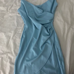 Ljusblå klänning med drapering - Säljer en superfin ljusblå klänning med draperad design. Den har smala axelband och en figurnära passform som ger en elegant look. Perfekt för sommarens fester eller en dag på stan. Klänningen är i mycket bra skick och redo för nya äventyr! 💙