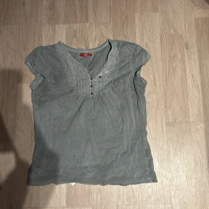 Grå ärmlös topp från Esprit - Säljer en stilren grå ärmlös topp från Esprit. Den har en v-ringad design med knappar framtill som ger en snygg detalj. Perfekt för både vardag och festliga tillfällen. Passar bra till jeans eller kjol!