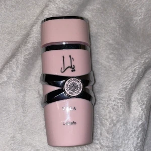 Parfym Yara från Lattafa - Säljer en elegant parfymflaska i ljusrosa med silverdetaljer från Lattafa. Flaskan har en unik form med arabiska bokstäver och en dekorativ emblem. Perfekt för den som vill ha en doft med stil och finess. Passar både till vardags och fest!