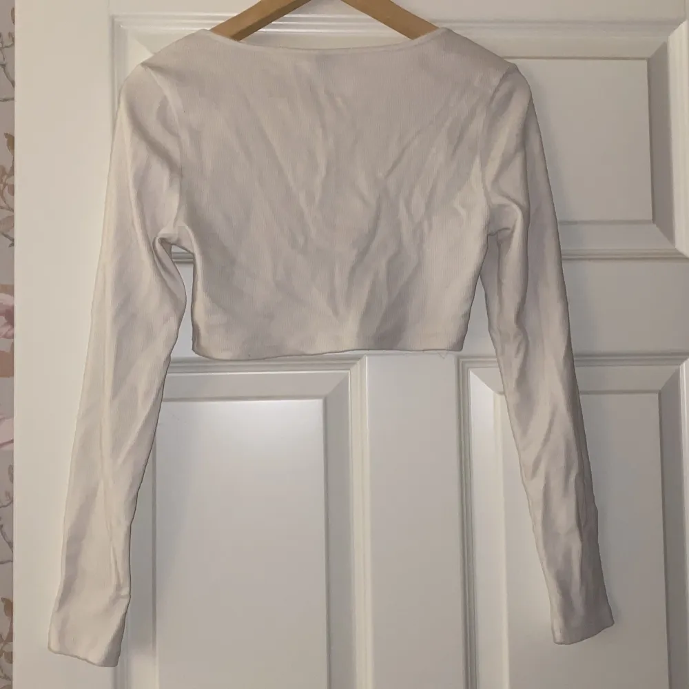 Säljer en vit croppad topp från H&M Divided i storlek M. Toppen har långa ärmar och knappar framtill, perfekt för en stilren look. Den är i bra skick och passar utmärkt till både vardag och fest.. Yläosat.