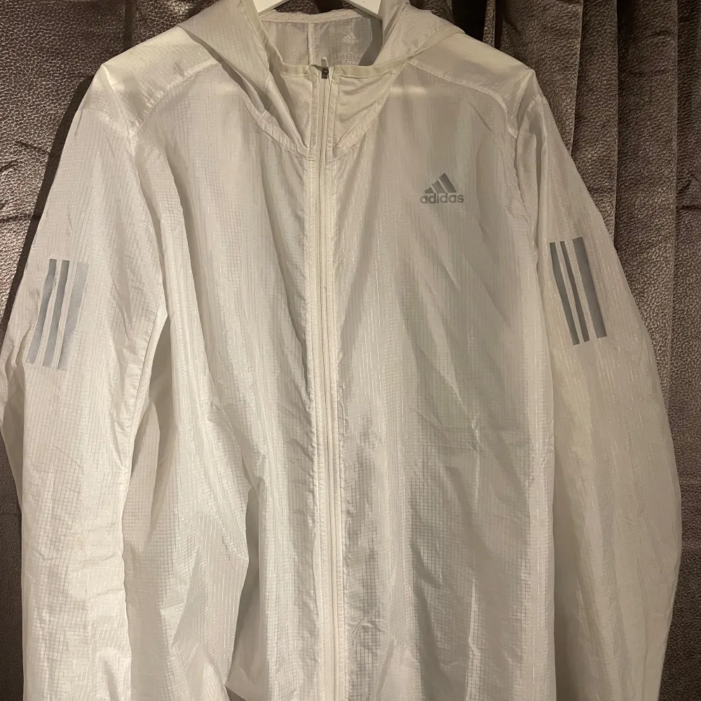 Säljer en vit vindjacka från Adidas i storlek L. Jackan har en dragkedja framtill och en huva. Perfekt för löpning eller andra utomhusaktiviteter. Den är i mycket bra skick och har de klassiska Adidas-ränderna på ärmarna. (pris ej hugget i sten). Jackor.