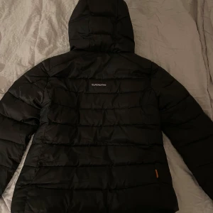 Vinterjacka - Säljer en svart jacka från Superdry i nyskick. Jackan har en huva och dragkedja framtill, perfekt för kalla dagar. Den är vadderad och har en mjuk insida för extra komfort. Märkeslogga på ärmen ger en snygg detalj. Passar perfekt för vintern och hösten! Storlek S🫶🏼