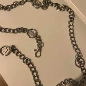 Silverfärgat Michael Kors kedjebälte med logodetaljer - Snyggt och trendigt silverfärgat kedjebälte med stora länkar och logodetaljer. Perfekt för att ge en extra touch till din outfit. Bältet har en praktisk karbinhake för enkel justering och passform. Passar både till vardags och festliga tillfällen.