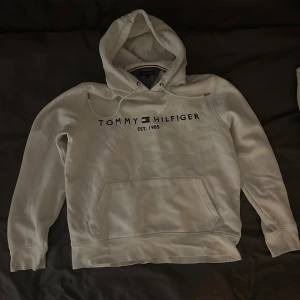 Vit hoodie från Tommy Hilfiger - Säljer en vit hoodie från Tommy Hilfiger som ser oanvänd ut. Den har en bekväm passform med långa ärmar och en praktisk magficka. Perfekt för en avslappnad stil eller kyliga dagar. 
