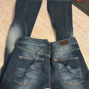 Lee jeans lågmidjade utåtsvängda  - Säljer ett par snygga mörkblå jeans från Lee i perfelt skick. De har väldigt fin design på bakfickorna och de är väldigt lågmidjade. 