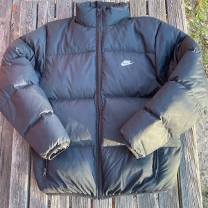 Svart dunjacka från Nike - Säljer en svart dunjacka från Nike i mycket bra skick. Jackan har en dragkedja framtill och två praktiska fickor med dragkedjor. Perfekt för kalla vinterdagar med sin pufferstil som håller dig varm och bekväm. Passar både till vardags och utomhusaktiviteter och är en perfekt julklapp🎅 Jackan köptes nyligen in för 2500 kr och har bara använts fåralet gånger😊storleken är small men passar även medium. Hör gärna av dig om du har frågor, jag skickar snabbt:) (priset kan diskuteras)