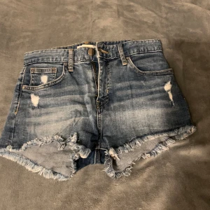 Blå jeansshorts med slitningar  - Säljer ett par snygga blå jeansshorts med slitna detaljer och fransig kant. Perfekta för sommaren. 
