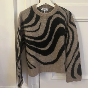 Tröja från & Other Stories - Säljer en supercool beige tröja med svart vågigt mönster från & Other Stories. Den är stickad och har långa ärmar, perfekt för höst och vinter. Tröjan är i mycket bra skick eftersom den nästan aldrig har kommit till användning tyvärr. Storlek S men funkar som M också!