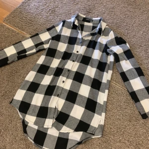 Svartvit rutig skjorta - Säljer en snygg svartvit rutig skjorta i storlek S. Skjortan har långa ärmar och knappar hela vägen ner. Perfekt för en avslappnad stil eller lager-på-lager look. Den är i bra skick och redo för nya äventyr!