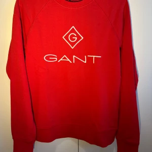 Röd sweatshirt från GANT - Säljer en snygg röd sweatshirt från GANT i mycket bra skick.Den har en klassisk design med GANT-loggan broderad på framsidan. Perfekt för både vardag och avslappnade tillfällen. Långärmad och gjord i mjukt material för extra komfort. Tröjan är använd ett fåtal gånger, har inga defekter🥰
