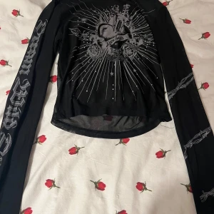 Svart långärmad mesh topp med tryck - Säljer en svart långärmad mesh topp med coolt tryck och texten 'Love Hurts'. Perfekt för en edgy look med detaljer på ärmarna. Materialet är lätt och bekvämt, perfekt för höst och vår. Passar bra till jeans eller kjol för en avslappnad stil.