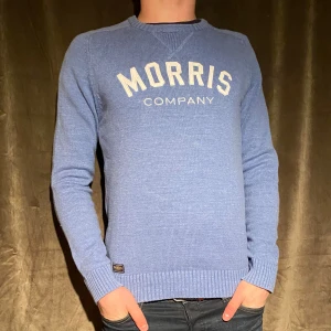 Stickad tröja - Morris - Säljer en snygg blå tröja från Morris med vit text på bröstet. Tröjan är i bra skick och har långa ärmar samt ribbade muddar vid ärmslut och nederkant. Perfekt för en casual look eller en chill dag ute. Passar bra till jeans eller chinos! Vid minsta fråga eller fundering hör av er🤝