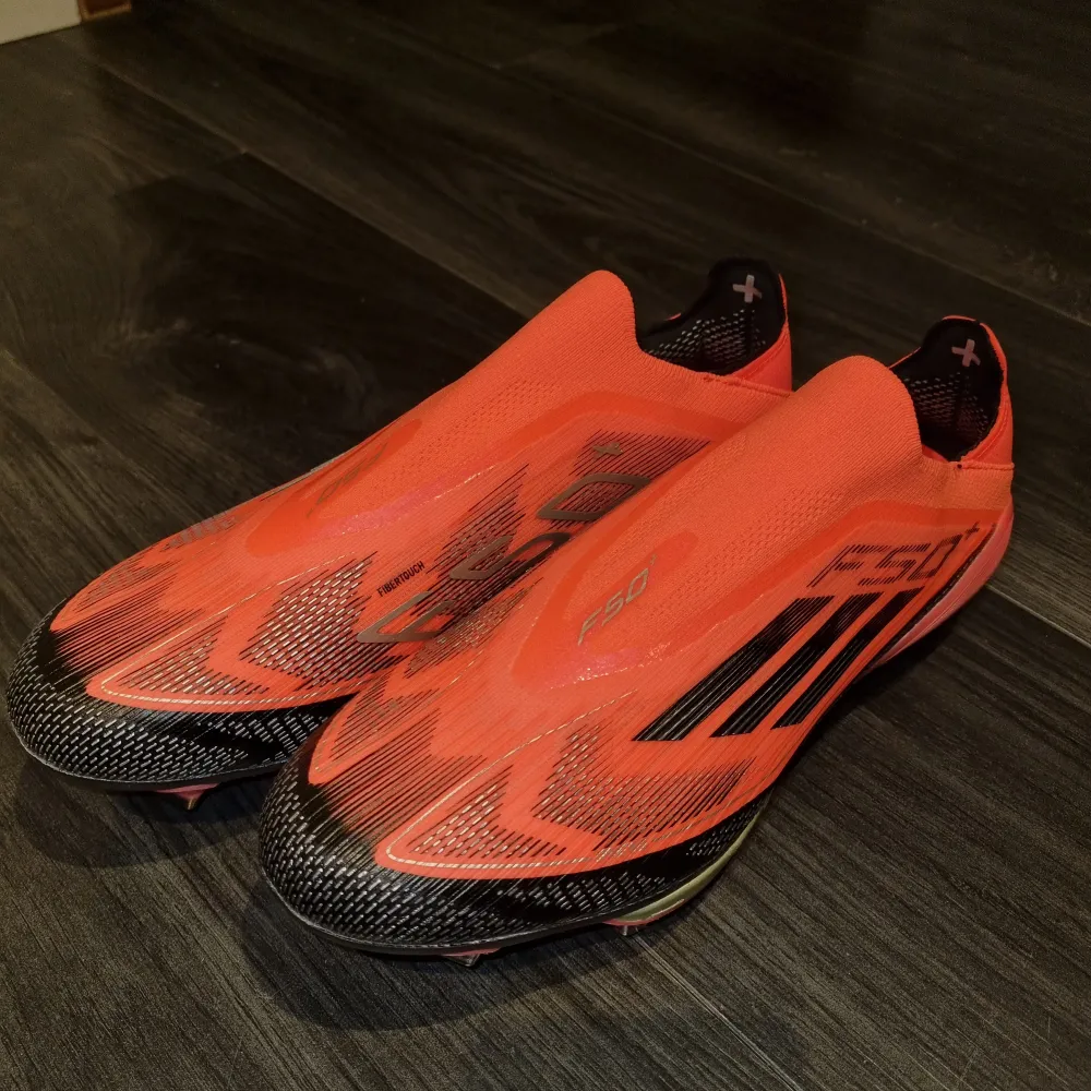 Säljer ett par grymma röda Adidas fotbollsskor i syntetmaterial. De har en cool design med svarta detaljer och är perfekta för fotbollsträning eller match. Skorna är i nytt skick och har en tight passform för bästa kontroll på planen. Perfekta för dig som vill sticka ut på planen!. Skor.