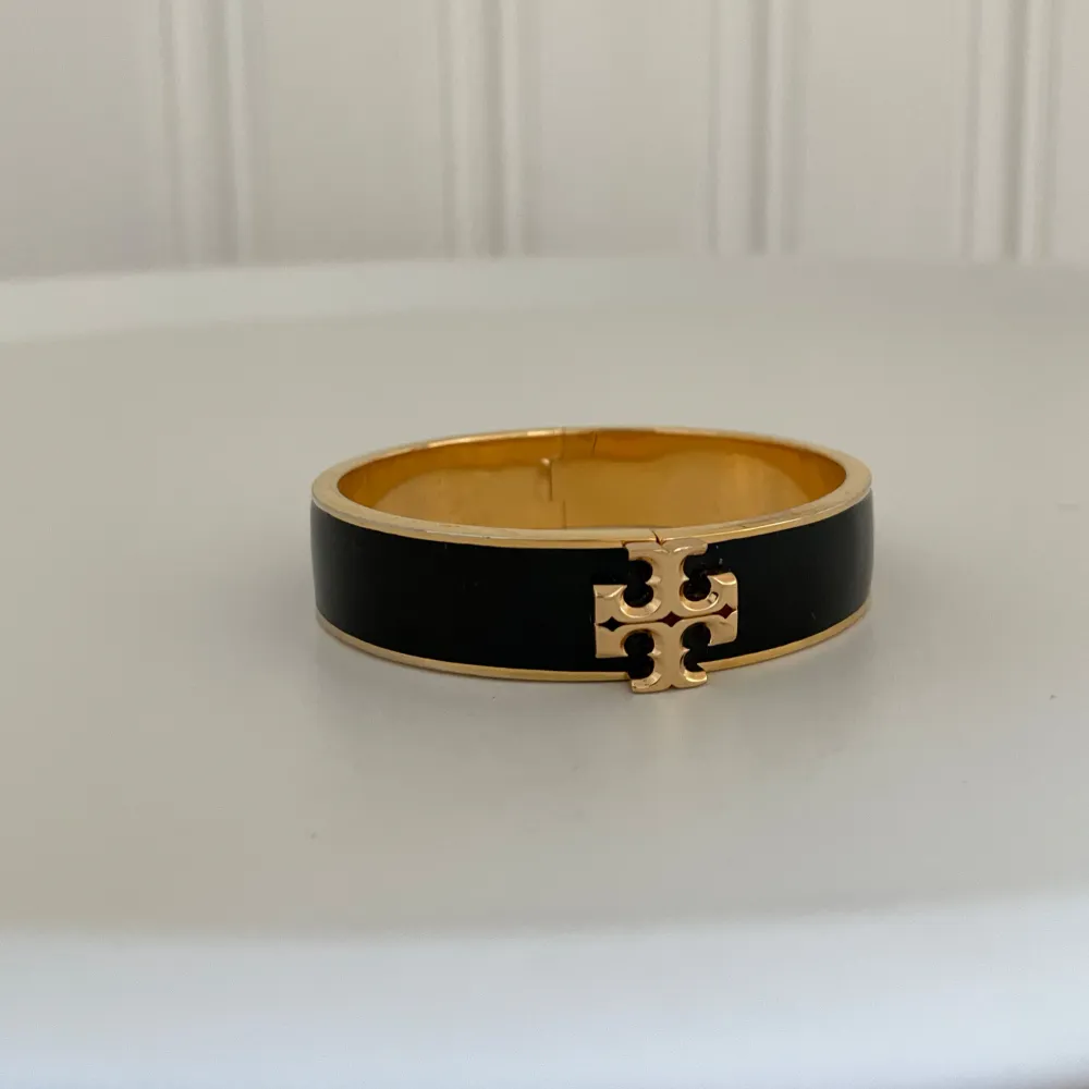 Snyggt armband i svart och guld med ett stilrent emblem i mitten. Perfekt för att ge en elegant touch till vilken outfit som helst. Armbandet har en enkel och modern design som passar både till vardags och fest. Nyskick slutsåld överallt mitt pris 2000kr inga repor/ som ny . Accessoarer.