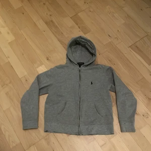 Grå hoodie från Polo Ralph Lauren - Säljer en grå zip-hoodie från Polo Ralph Lauren i storlek 10-12 år M. Den är i bra skick och har tagits väl hand om! 