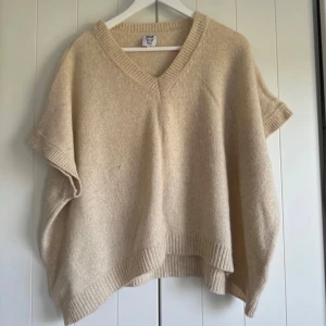 Beige stickad tröja - Mysig beige stickad tröja/poncho med v-ringning. Perfekt för kyliga höst- och vinterdagar. Den har en lös passform och ribbade kanter som ger en stilren look. Ett måste för garderoben om du gillar lager-på-lager-stil! Storlek S från märket Stajl. 
