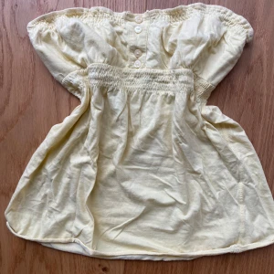 Gul axelbandslös vintage topp - Söt gul axelbandslös topp med smockdetaljer vid bysten och knappar framtill. Perfekt för sommardagar eller en avslappnad fest. Toppen har en luftig passform och är mjuk och skön att ha på sig! Köpt utomlands och har heller ingen storlek, skulle säga att den är mellan S/M😇 Toppen är mer gul i verkligeheten