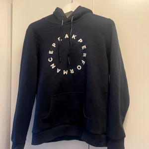 Mörkblå hoodie från Peak Performance - Säljer en mörk blå hoodie från Peak Performance i bra skick. Den har en stor logga i vitt på framsidan och en  magficka. Perfekt för höst och vinter, Passar både till vardags och träning!