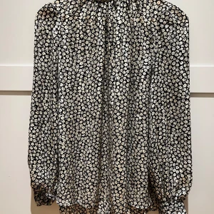 Blus  - En fin blus med blommor i botten , tre knappar i nacken och snygg stående krage . Även knappar runt armleden som ytligare en fin detalj . 