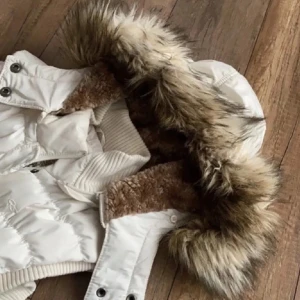 Vit väst med päls från QS by s.Oliver - Säljer en superfin vit quiltad väst från QS by s.Oliver i storlek S. Den har päls runt huvan och stängs med dragkedja och knappar. Perfekt för hösten